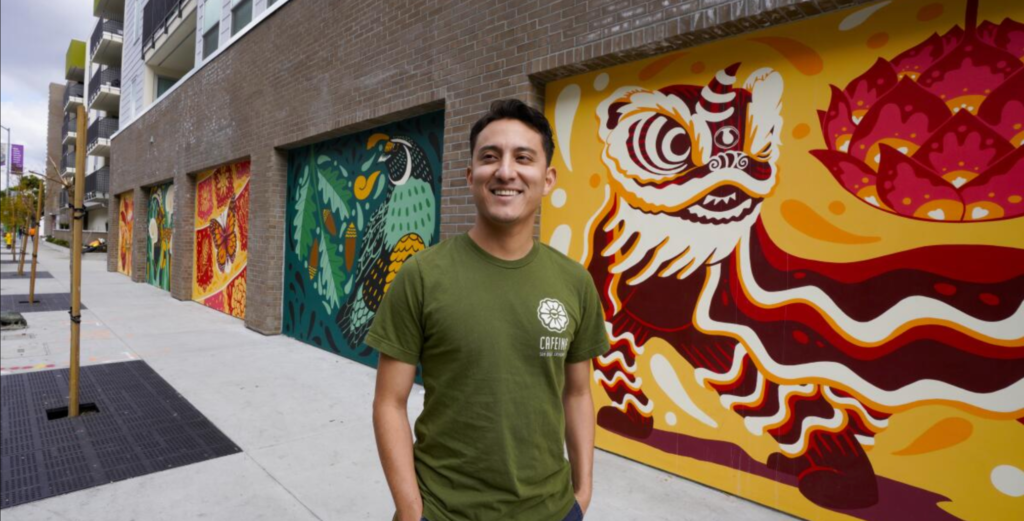 Artist Josue standing in front of his mural in City Heights.